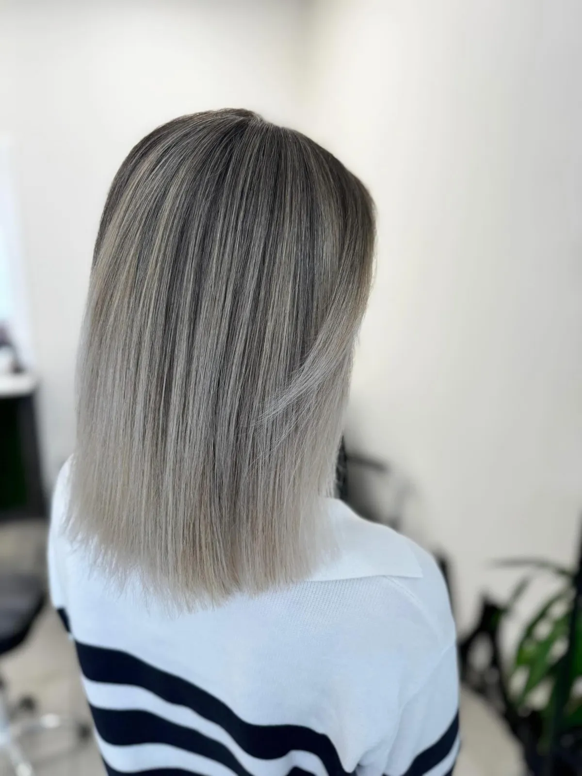 Pelēcīgi blonds, gluds garš bobs ar tumšākām saknēm, skats no aizmugures